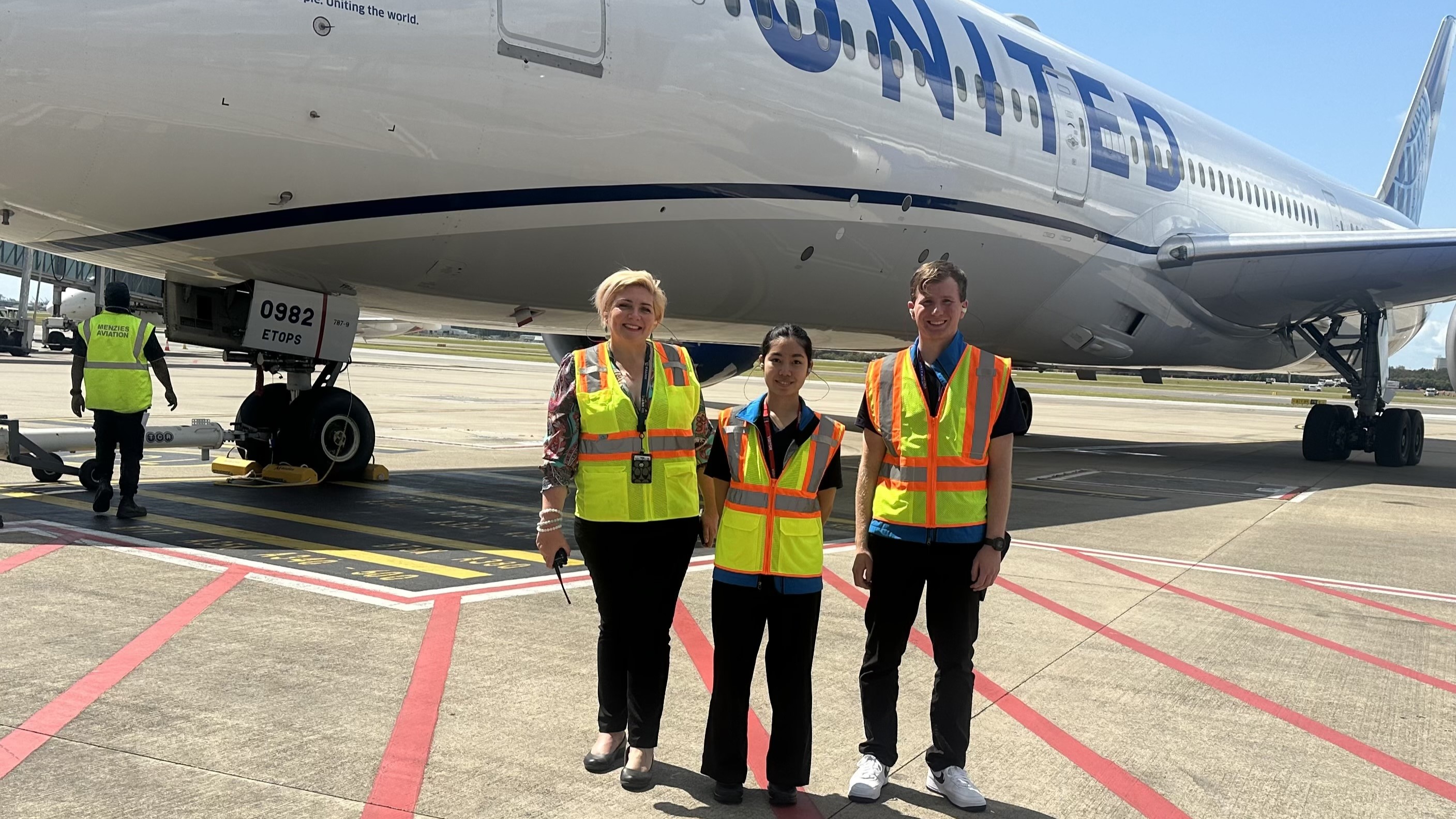 Two students and a United Airlines staff member standing in front of a United Airlines plane