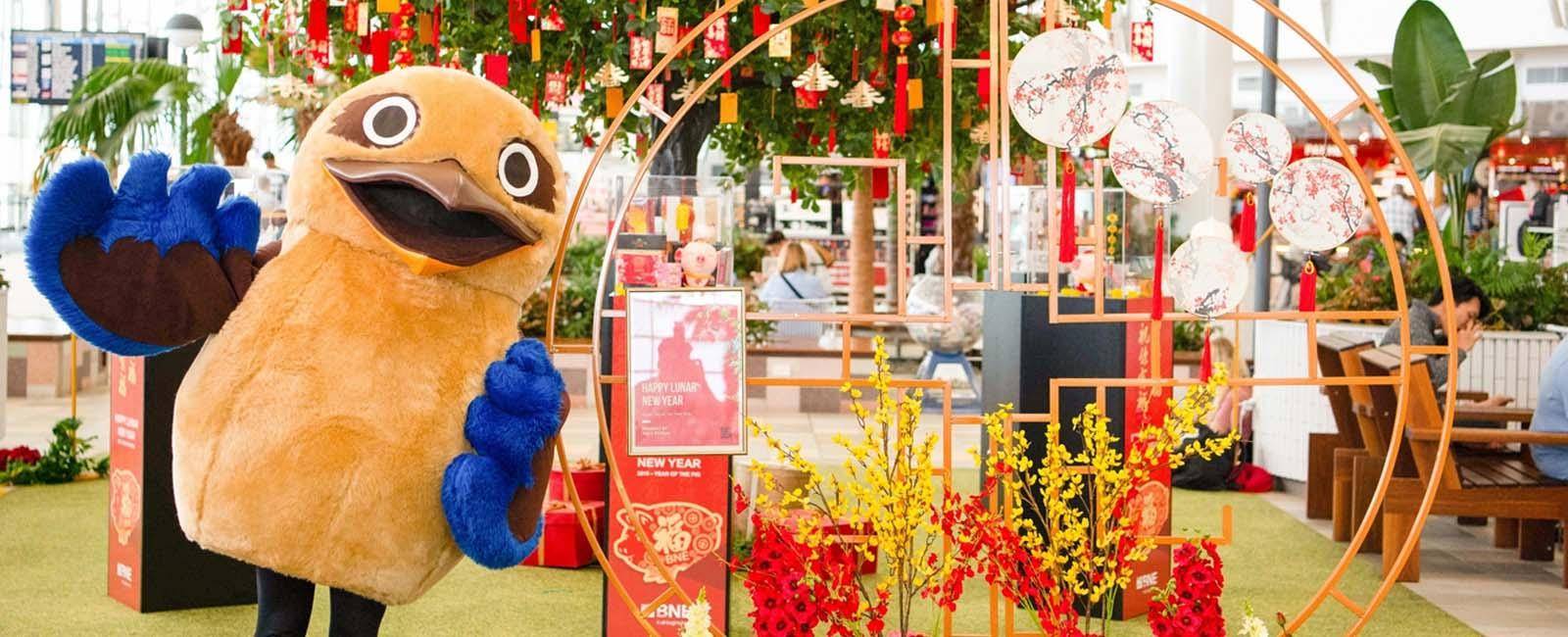 A person dressed in a kookaburra costume next to lunar new year decorations